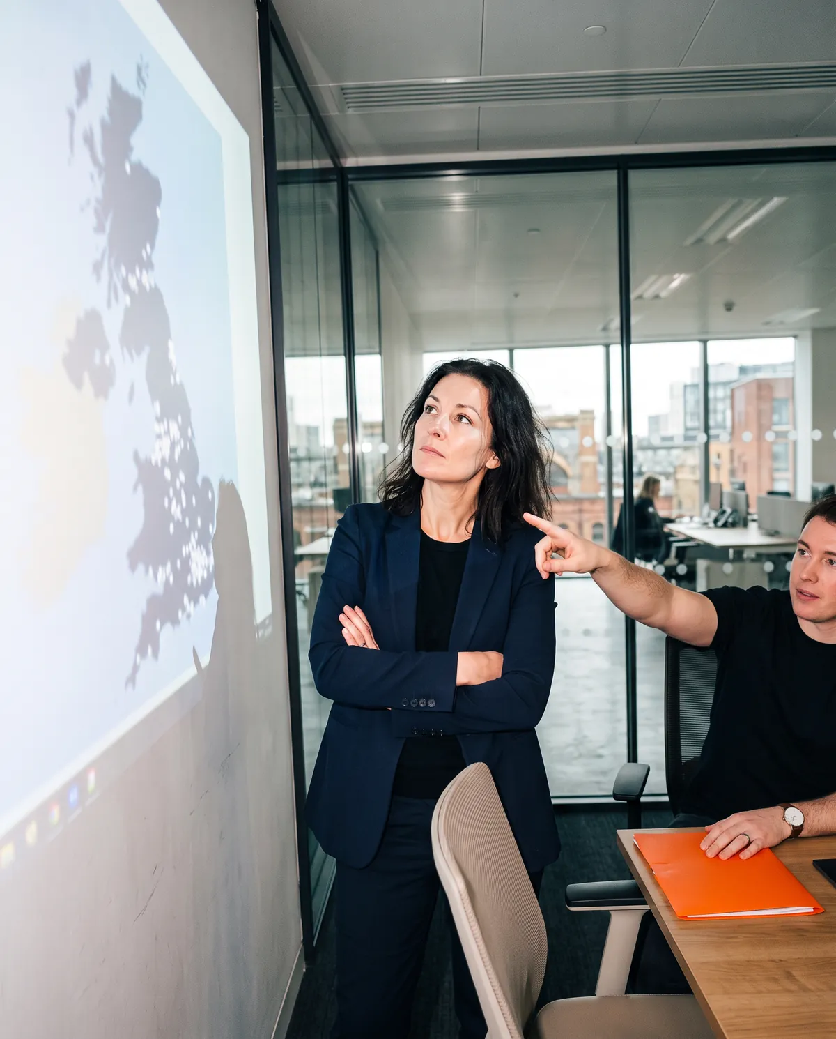 Two acquirers in a glass meeting room looking at a map of founder-owned businesses on a wall screen